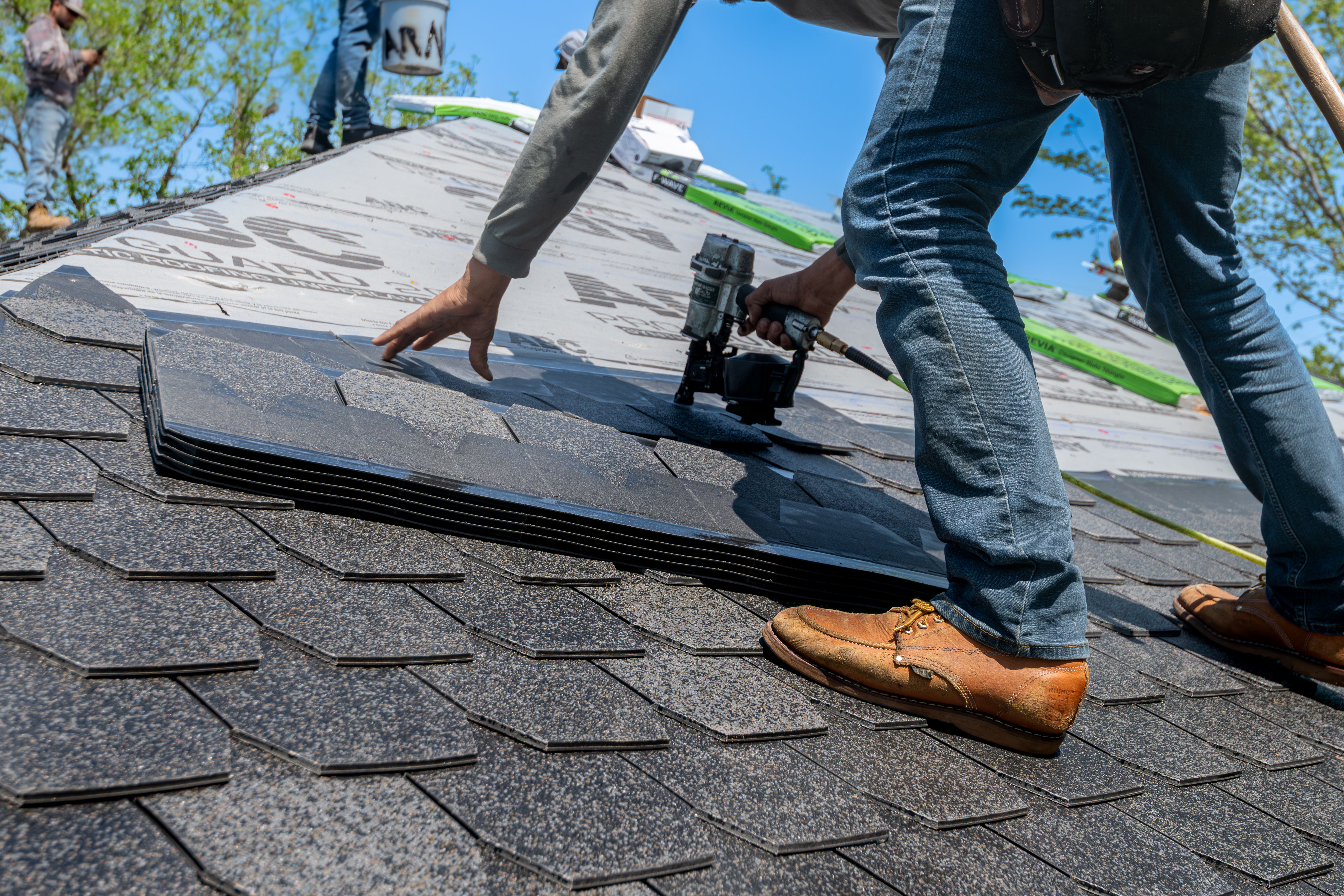 A roofer installing asphalt shingles with a nail gun